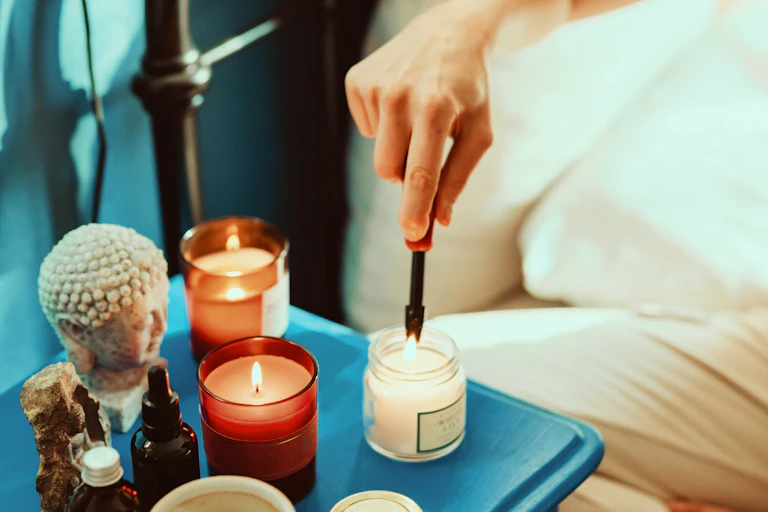 A person's hand lighting several scented candles on a blue bedside table