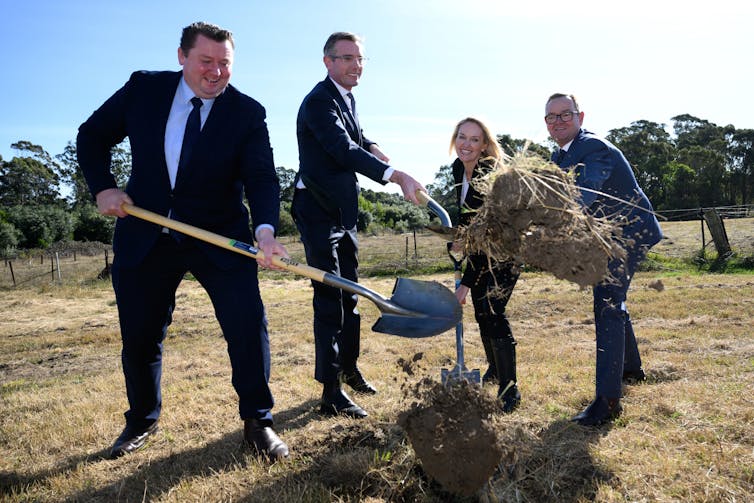 Four people in suits toss newly turned sods towards the camera