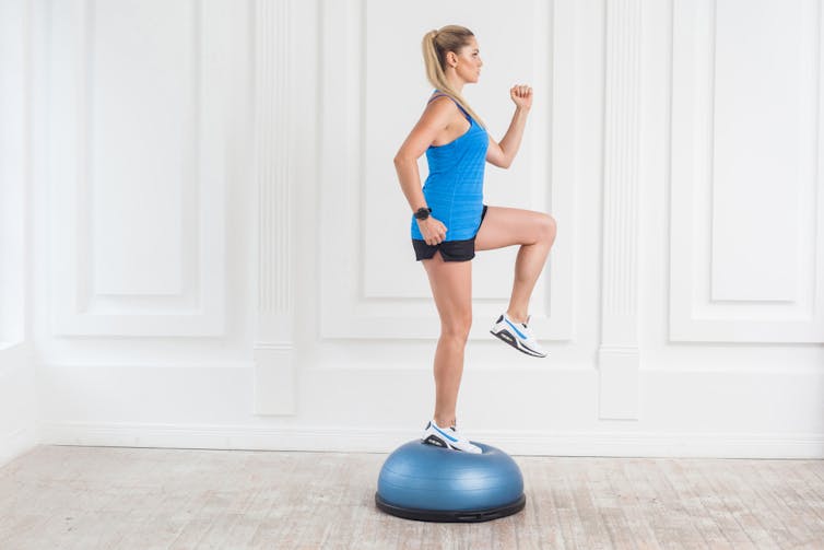 A woman balances on a wobble disc.