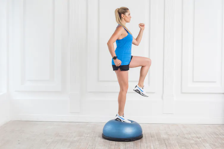 A woman balances on a wobble disc.