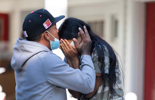 Man holds head of crying woman and kisses her forehead.