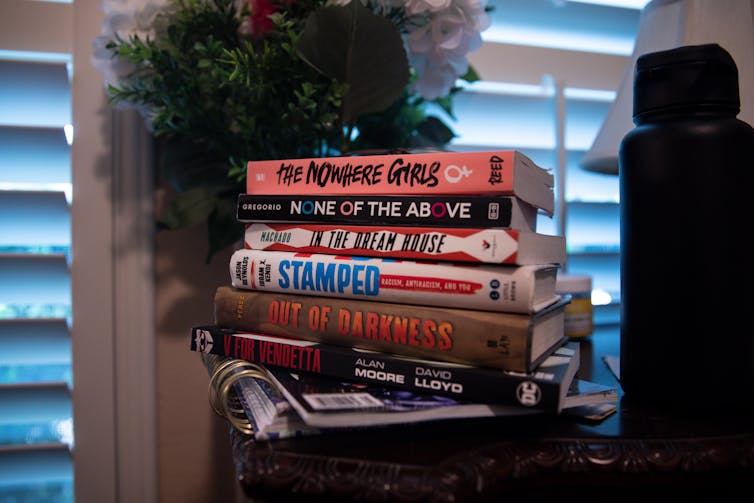 Stack of six books, including The Nowhere Girls and None of the Above, on a dresser.