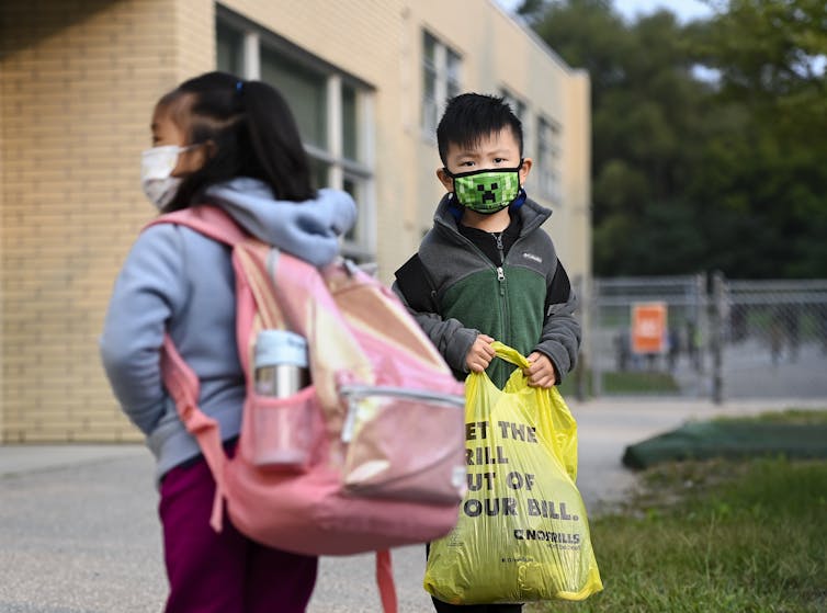 Children standing outside a school wearing masks.