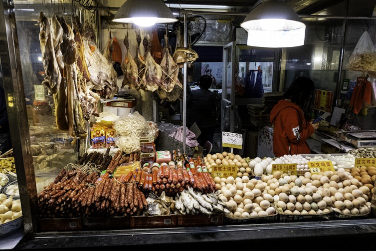 Vue de stands chargés d’œufs, saucisses, poissons crus, animaux dépecés… 