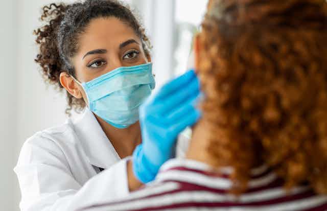 Doctor wearing a mask and gloves examines a patient.