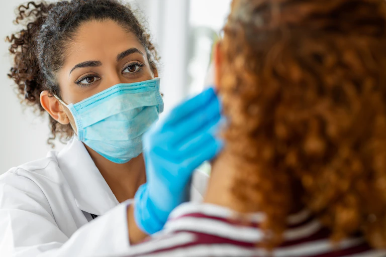 Doctor wearing a mask and gloves examines a patient.