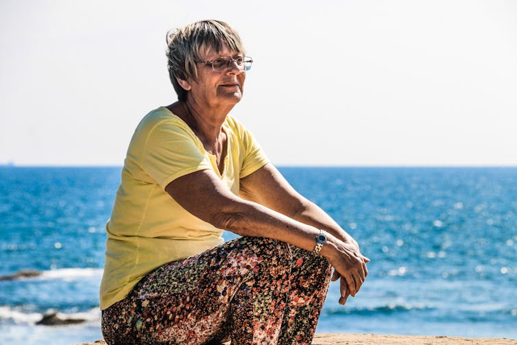 Older woman sits near the beach