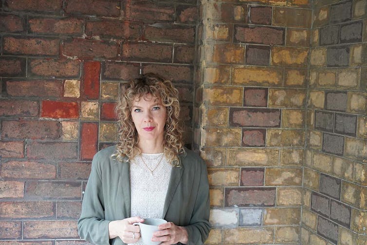 a woman with curly blonde hair, holding a coffee cup and wearing a cardigan