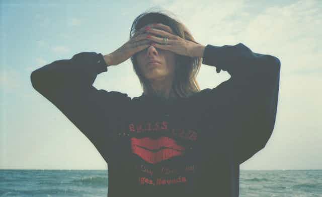 Girl in hoodie with hands over her eyes, against sea and sky