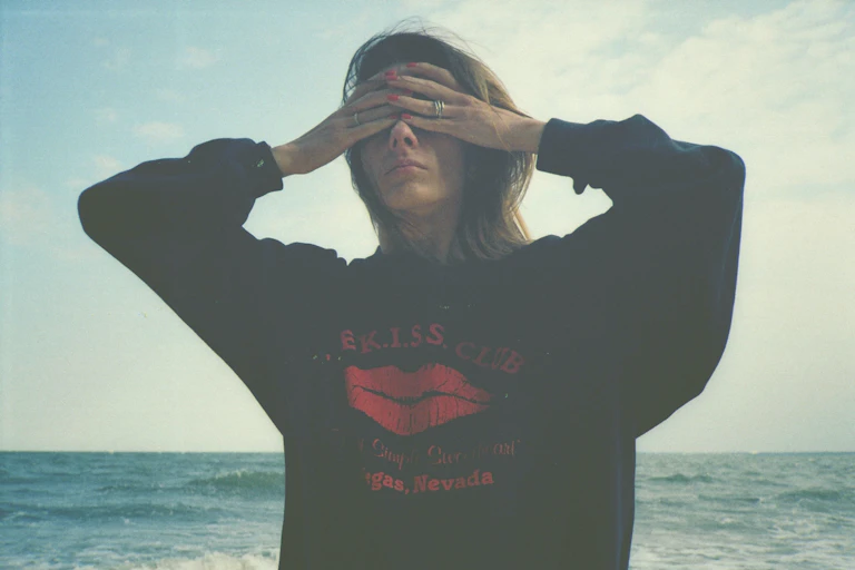 Girl in hoodie with hands over her eyes, against sea and sky