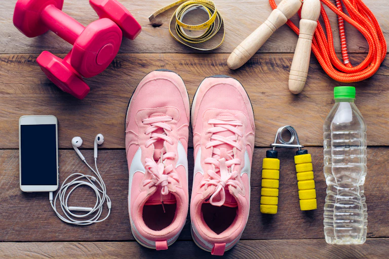 An overview of exercise equipment needed for a workout, such a trainers, dumbbells, water and a phone and earplugs.
