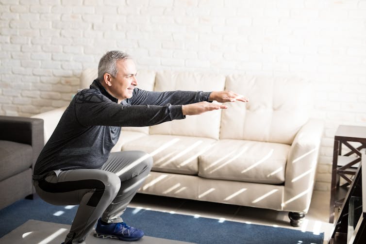 An older man performs a squat.