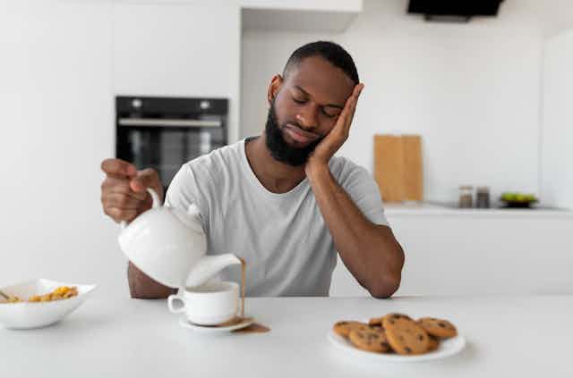 Tired man, pouring tea and missing the cup.