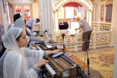 Women wearing white head covering plays keyboard and sings inside temple