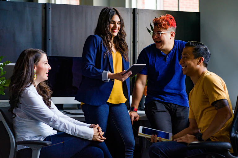 A group of students seen with devices, communicating and smiling.