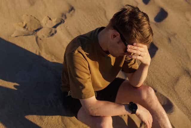 Un jeune homme se tient la tête dans un paysage désertique.