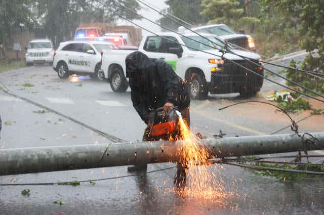 A man cuts a downed power pole with a chain saw in the rain