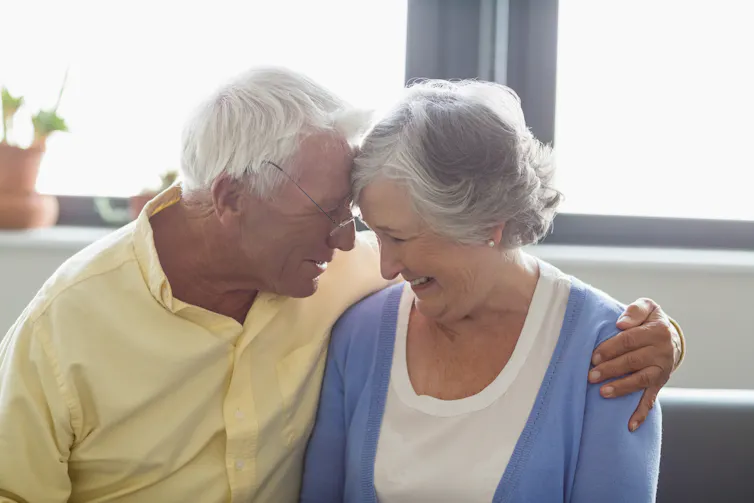 An older couple sitting on a sofa looking at each other, the man with his arm around the woman.