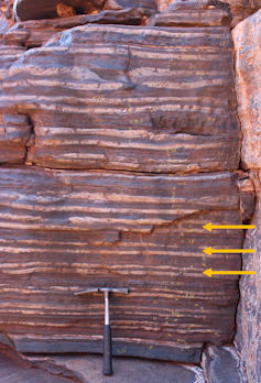 Rhythmically alternating layers of white, reddish and/or blueish-grey rock at an average thickness of about 10 cm (see arrows). The alternations, interpreted as a signal of Earth’s precession cycle, help us estimate the distance between Earth and the moon 2.46 billion years ago. (Frits Hilgen)