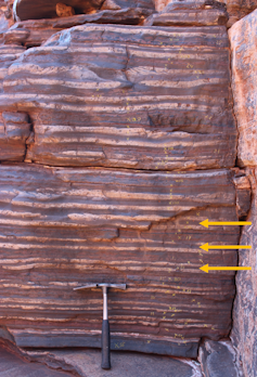 Rhythmically alternating layers of white, reddish and/or blueish-grey rock at an average thickness of about 10 cm (see arrows). The alternations, interpreted as a signal of Earth’s precession cycle, help us estimate the distance between Earth and the moon 2.46 billion years ago. (Frits Hilgen) Rhythmically alternating layers of white, reddish and/or blueish-grey rock at an average thickness of about 10 cm (see arrows). The alternations, interpreted as a signal of Earth’s precession cycle, help us estimate the distance between Earth and the moon 2.46 billion years ago. (Frits Hilgen)