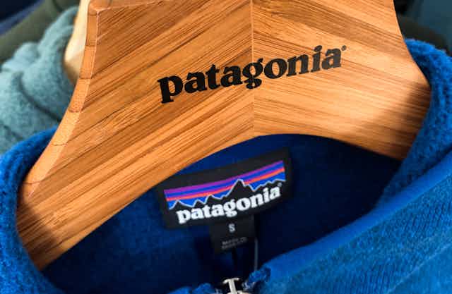 A wooden hanger emblazoned with the patagonia brand name, on which a patagonia fleece jacket hangs.