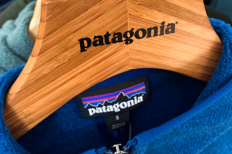 A wooden hanger emblazoned with the patagonia brand name, on which a patagonia fleece jacket hangs.