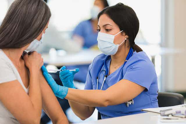 Close-up photo of a female nurse wearing a mask and giving a shot to an adult woman at a vaccination center.
