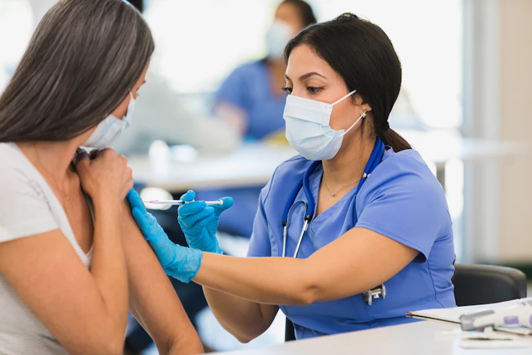 Close-up photo of a female nurse wearing a mask and giving a shot to an adult woman at a vaccination center.