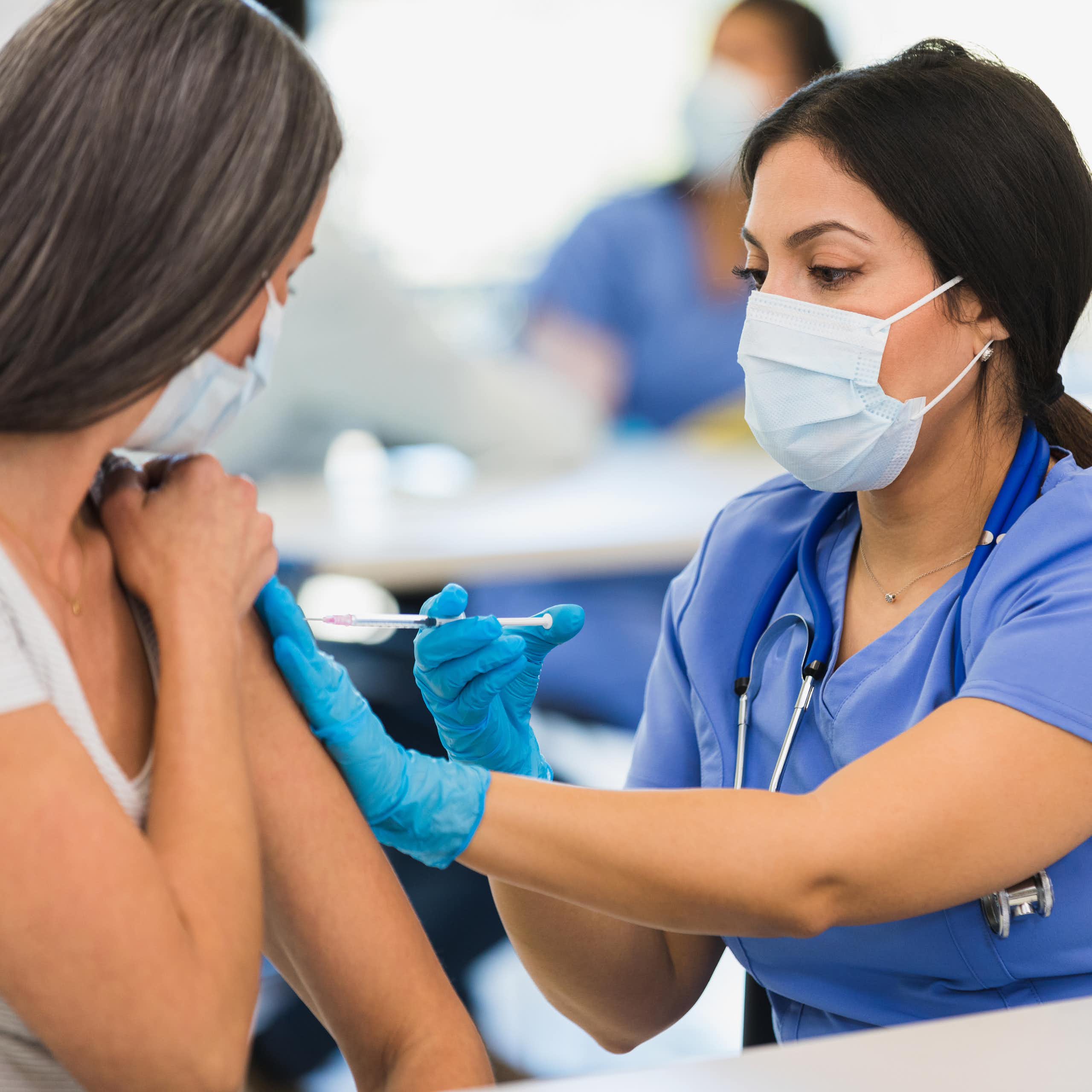 Close-up photo of a female nurse wearing a mask and giving a shot to an adult woman at a vaccination center.