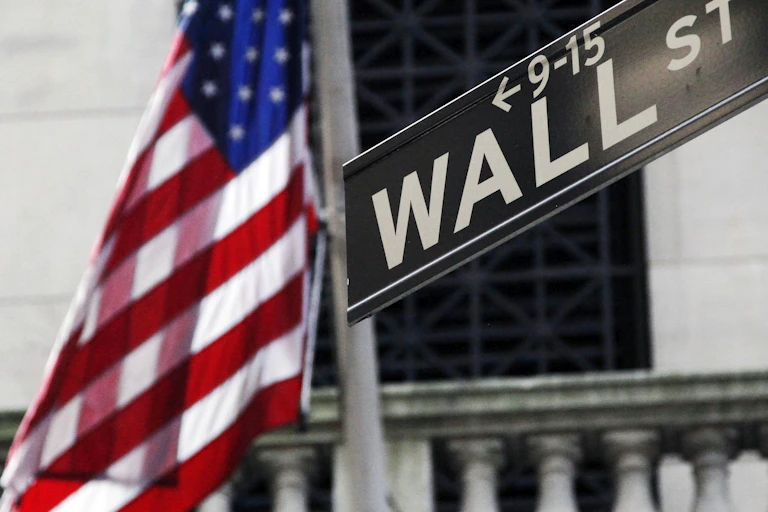 a us flag waves next to a sign reading wall street