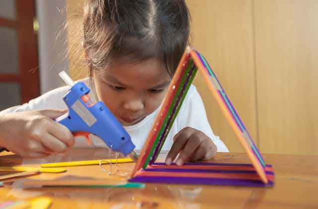 A child glues colourful paddle-pop sticks into a triangle with a glue gun.