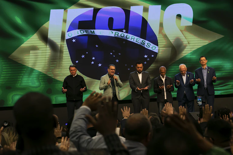 Six men pray on a stage in front of an image of the Brazilian flag.