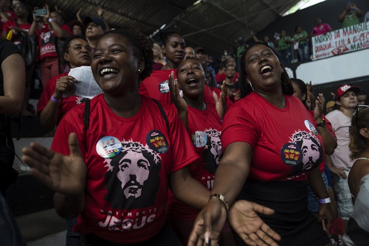 Several women in red T-shirts with pictures of Jesus dance and sing at a rally.