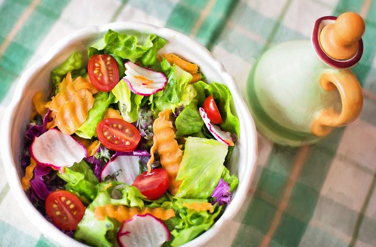 A salad sits on a table near an olive oil carafe