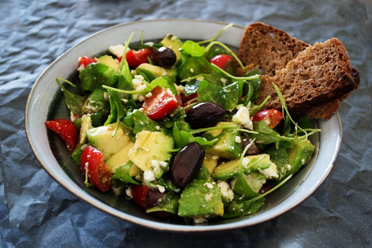 A salad with avocado and brown bread sits on a table.