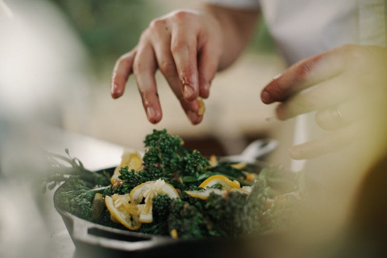 A person tears up kale leaves to drop them in a salad.