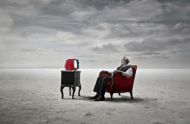 Dreamscape: old man watching TV on a sandy plain.