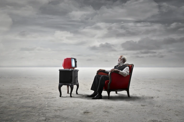 Dreamscape: old man watching TV on a sandy plain.