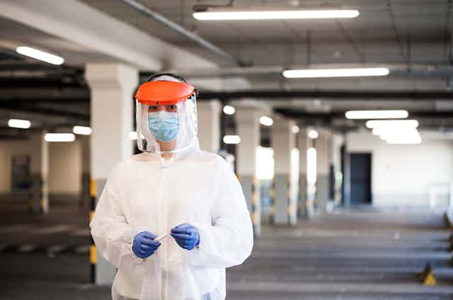 A healthcare worker dressed in full PPE in a carpark.