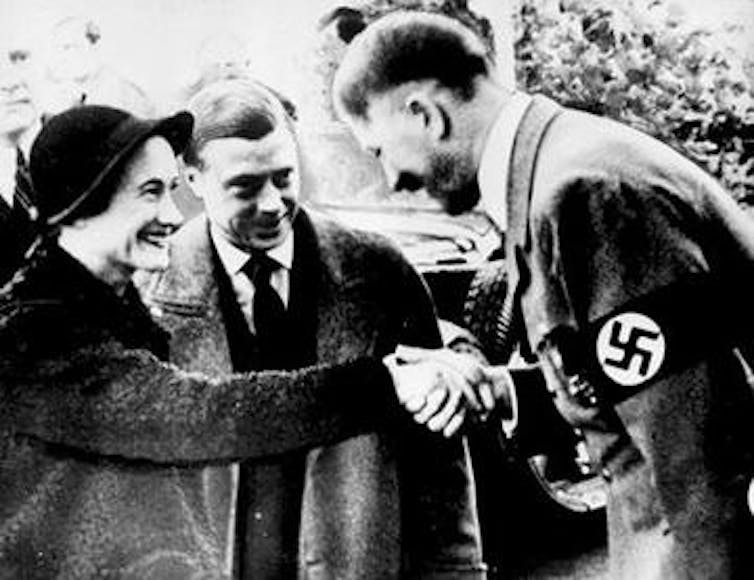 The duchess of WIndsor (formerly Mrs Wallis SImpson) shakes hands with Adolf Hitler as her husband, the duke of Windsor (formerly KIng Edward VIII) looks o smiling.