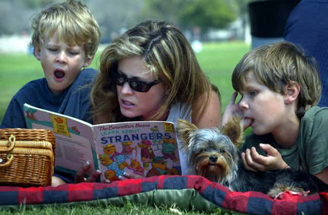 Woman reads a picture book to her two children in a park.