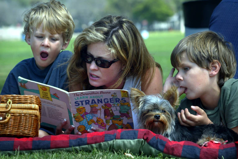 Woman reads a picture book to her two children in a park.