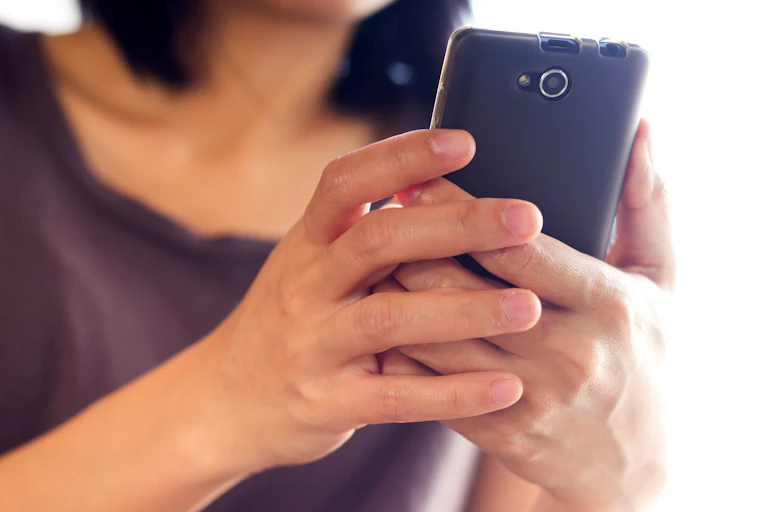 Une jeune femme tient son téléphone à deux mains