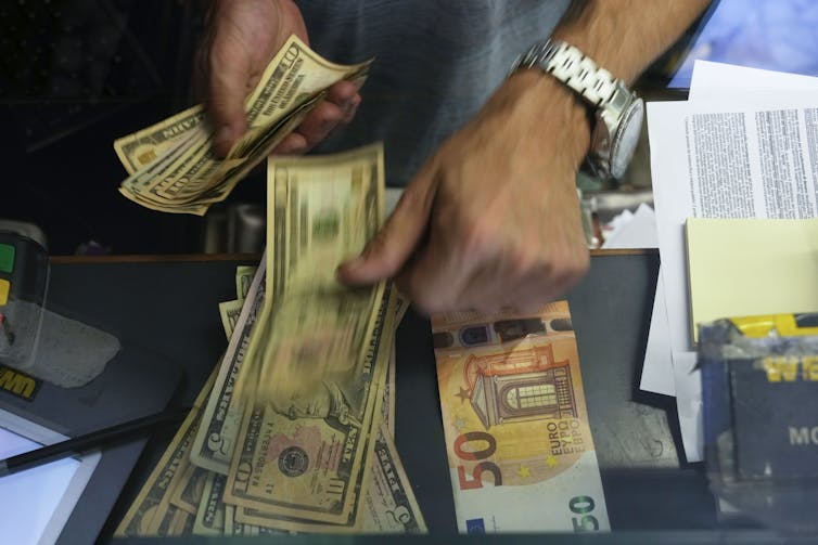 Hands hold and pick up US dollar bills next to euros at an exchange counter