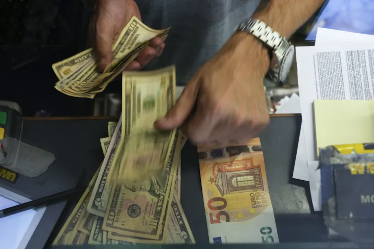 Hands hold and pick up US dollar bills next to euros at an exchange counter