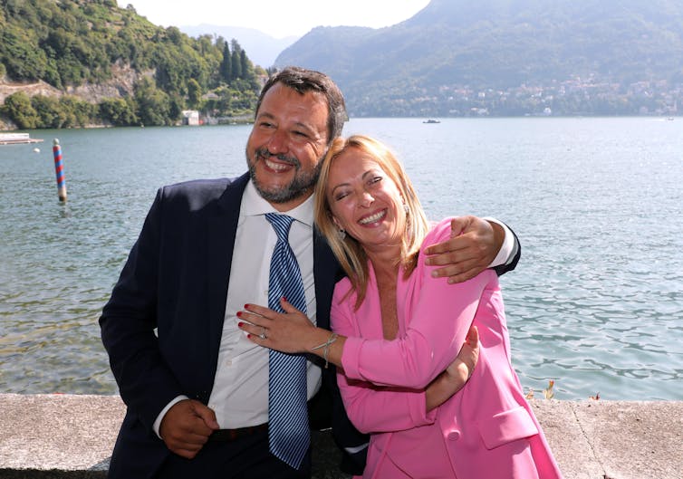 Matteo Salvini ir Giorgia Meloni kartu pozuoja nuotraukai priešais ežerą.
