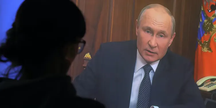La silueta de una mujer viendo a Vladimir Putin en la televisión
