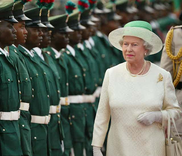 a line up of soldiers in green next to the queen in white with a green hat 