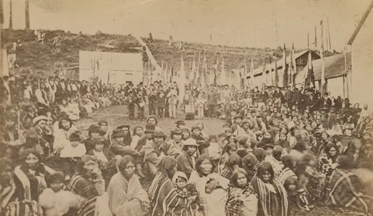 An old photo shows a large group of people sitting outside in a large circle.