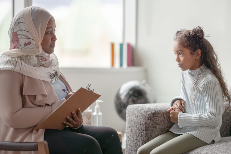 woman in chair with clipboard across from girl on couch